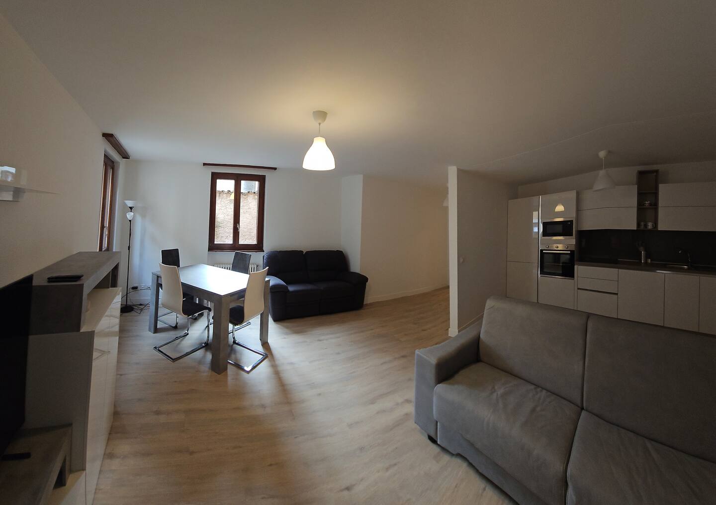 Living room with a dining table, couch, sofa, wooden floor, ceiling light, windows, kitchen