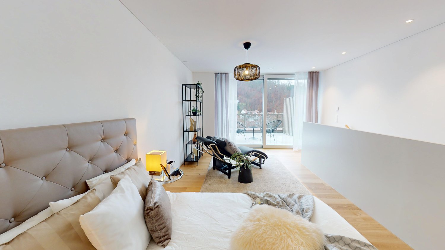 modern bedroom with a large bed, balcony, wooden floor, white walls, decorative items, and a view of the outside