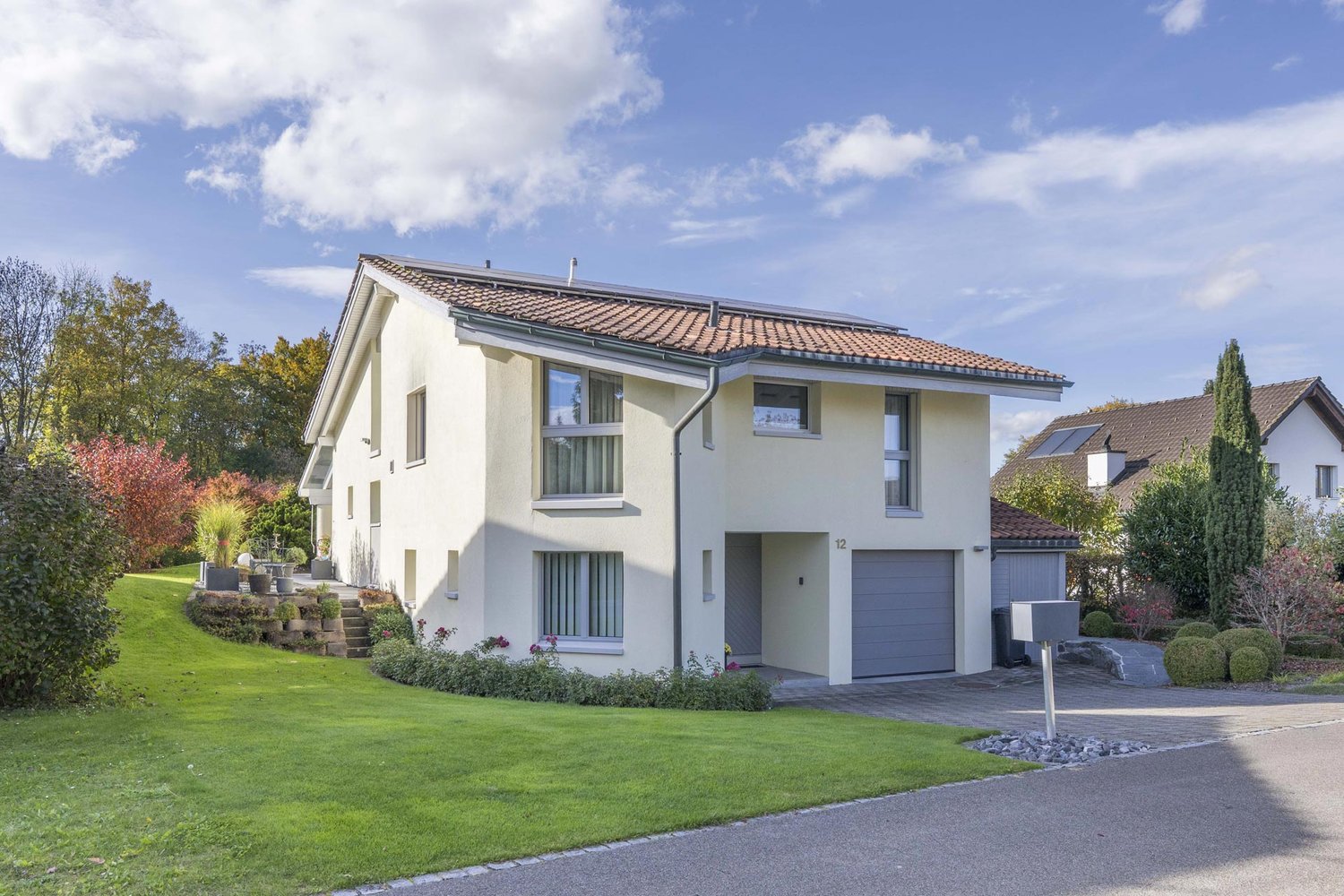 Two-story house, white walls, solar panels, grey garage, well-kept garden, driveway