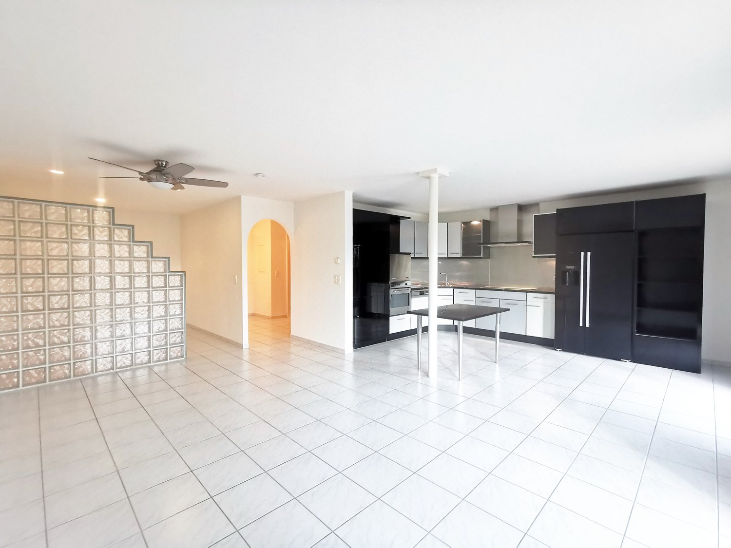 tiled floor, white walls, large arched doorway, black kitchen cabinets, modern kitchen setup, ceiling fan
