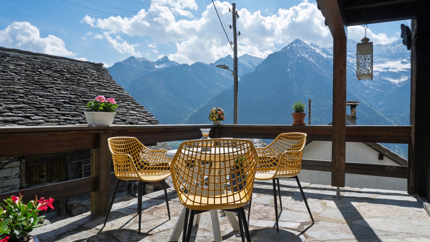 yellow chairs, round table, wooden railing, potted plants, mountain view