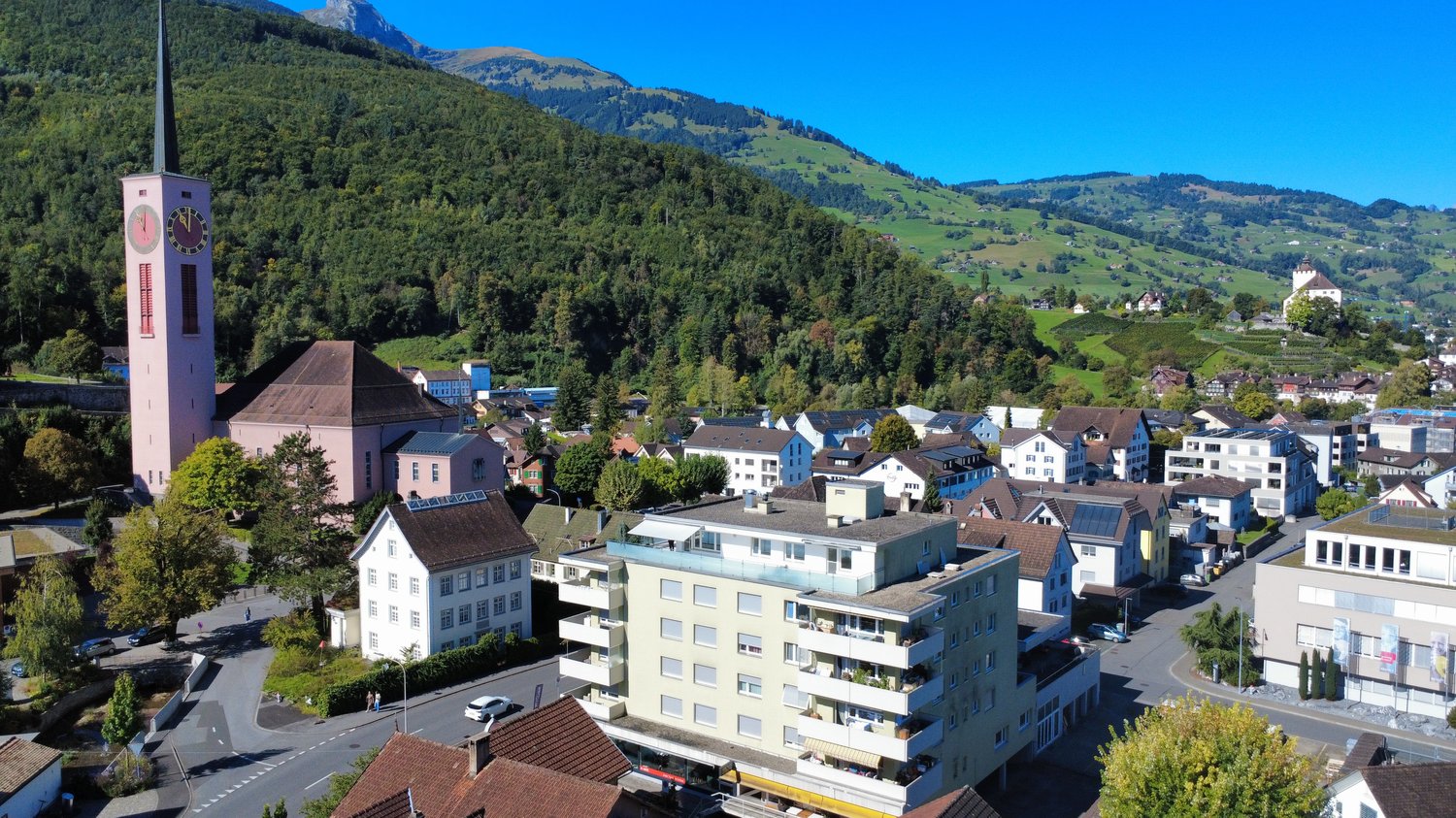 Overview of a town with many buildings, green hills, and a tower in the center