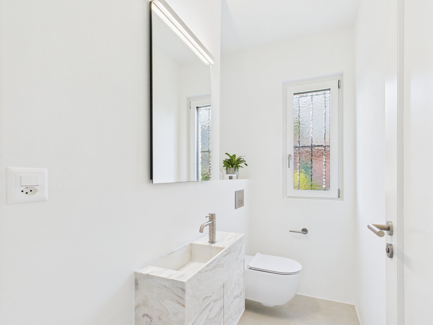 all white, marble vanity, toilet, sink, glass window, plant