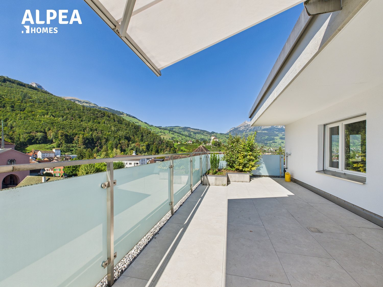 Glass railing balcony with tile flooring, overlooking a scenic mountain view