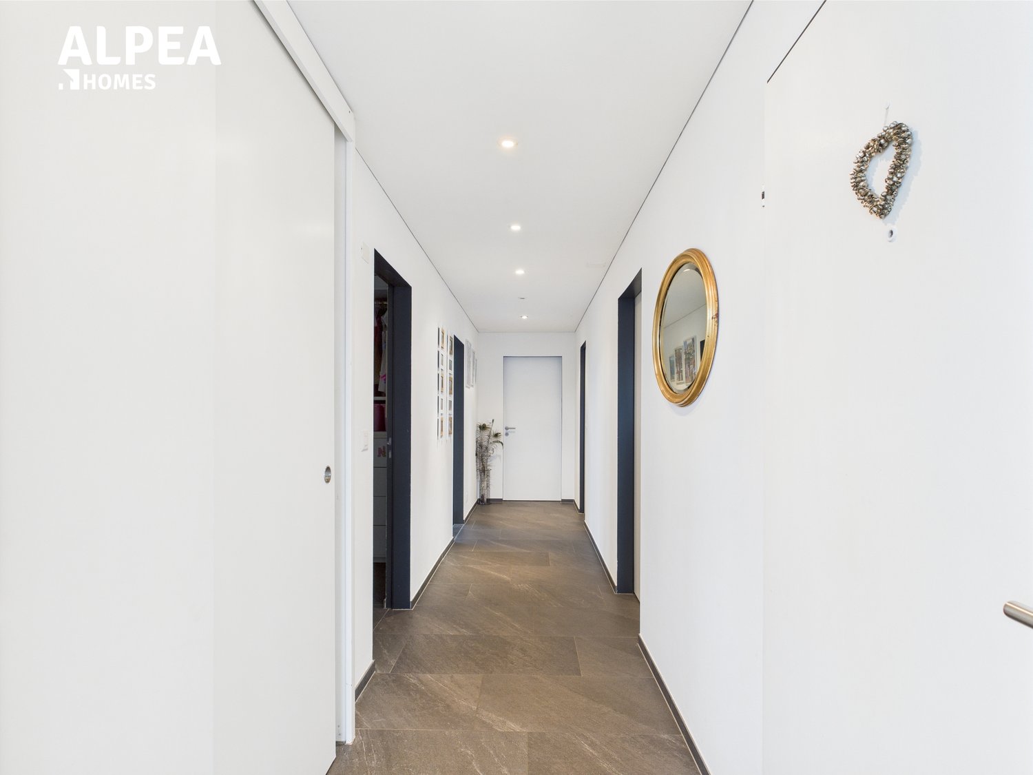 White walls, tiled floor, two doors with black frames, mirror, plant