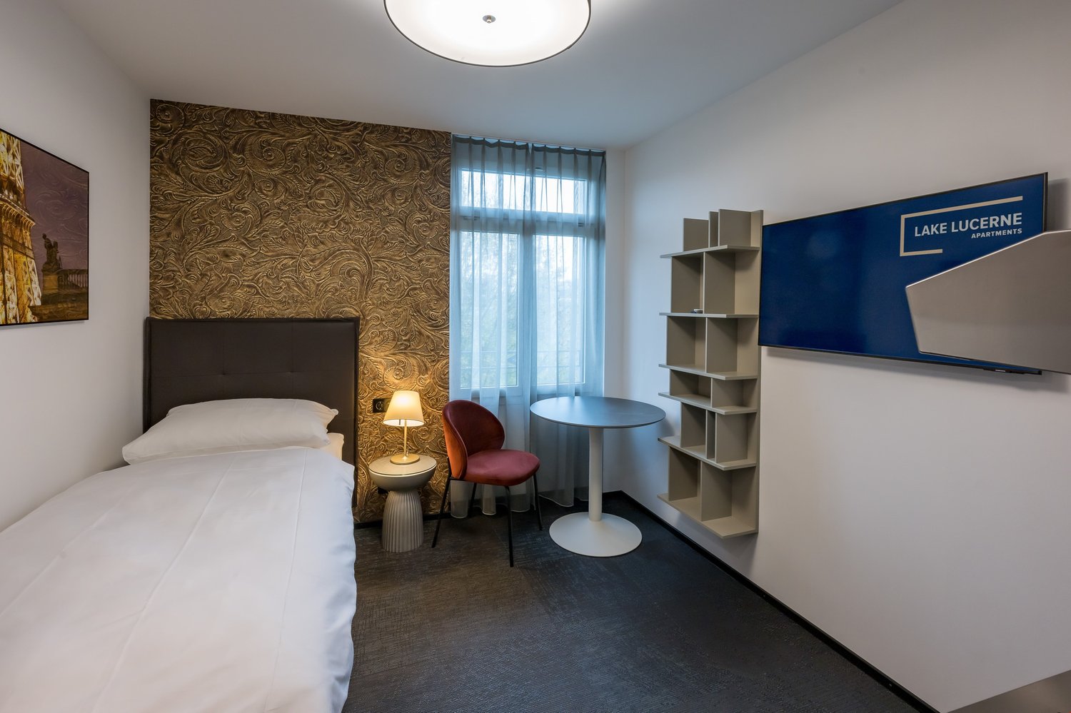 Small room with bed, bedside table, desk, chair, lamp, wall decoration, curtain, shelf, wall mounted sign