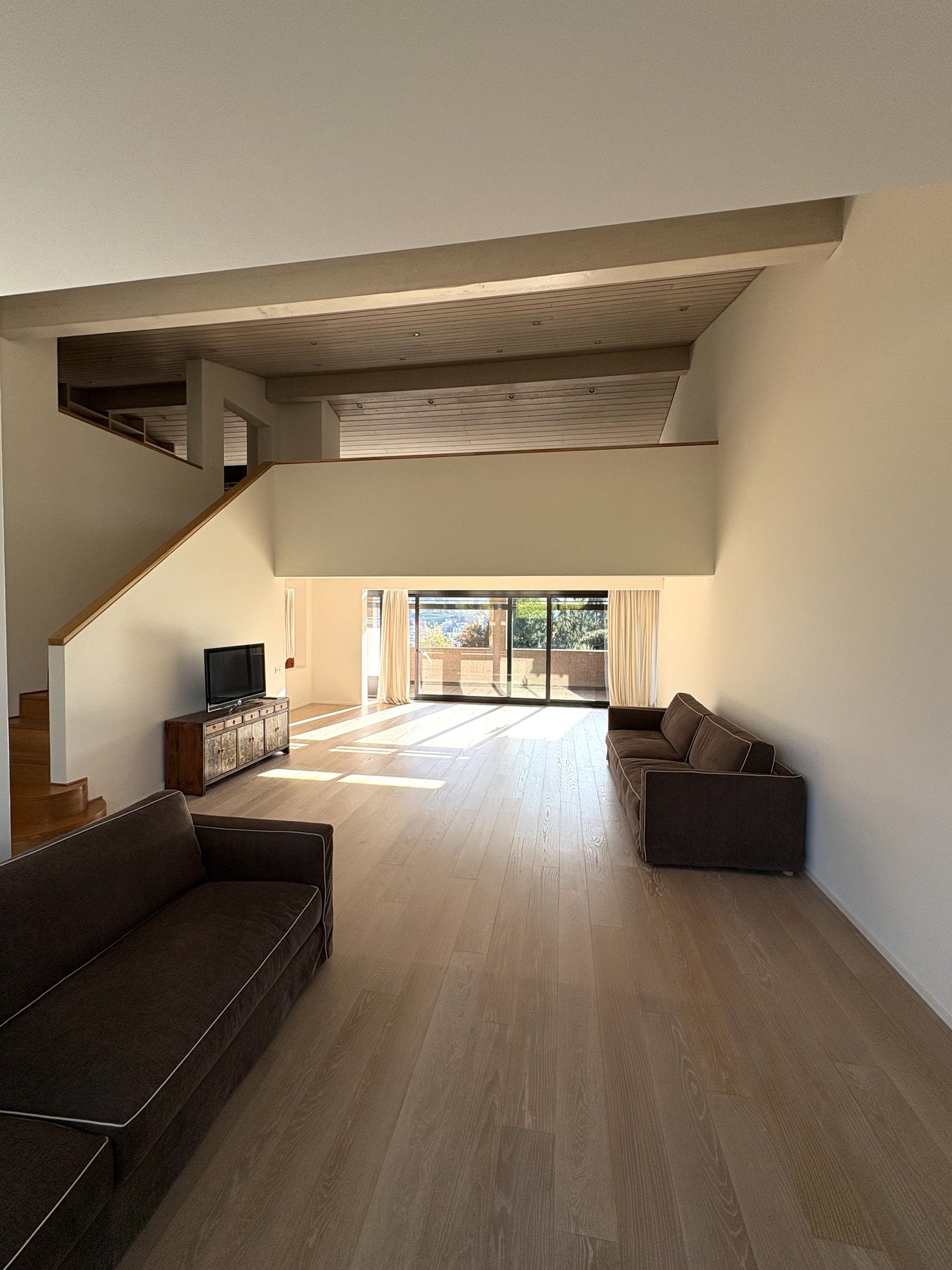 spacious room, wooden floors, modern furniture, large windows, living room setting, staircase