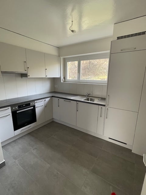 Spacious L-shaped kitchen with white cabinets, grey countertops, and grey tile flooring. The kitchen includes a built-in dishwasher.
