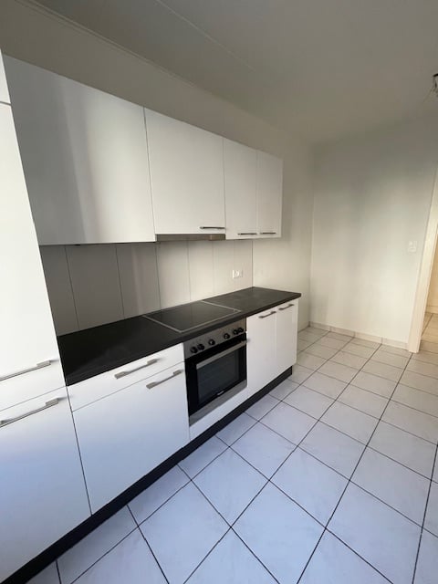 Modern kitchen with white cabinets, black countertops, white tiles, electric stove, oven, open layout, no visible washing machine or dishwasher