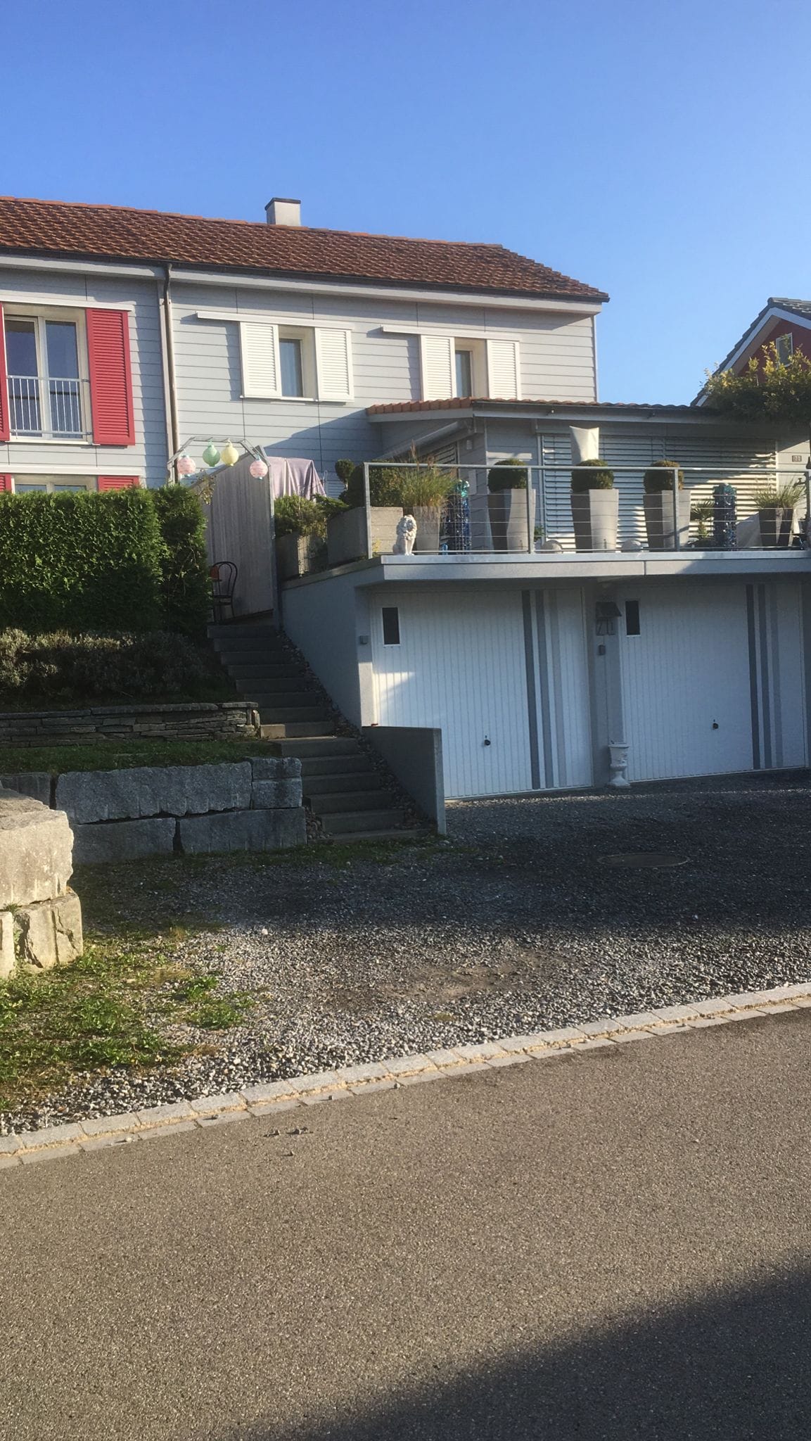 House with two garages, terrace, gravel driveway, shrubs and greenery