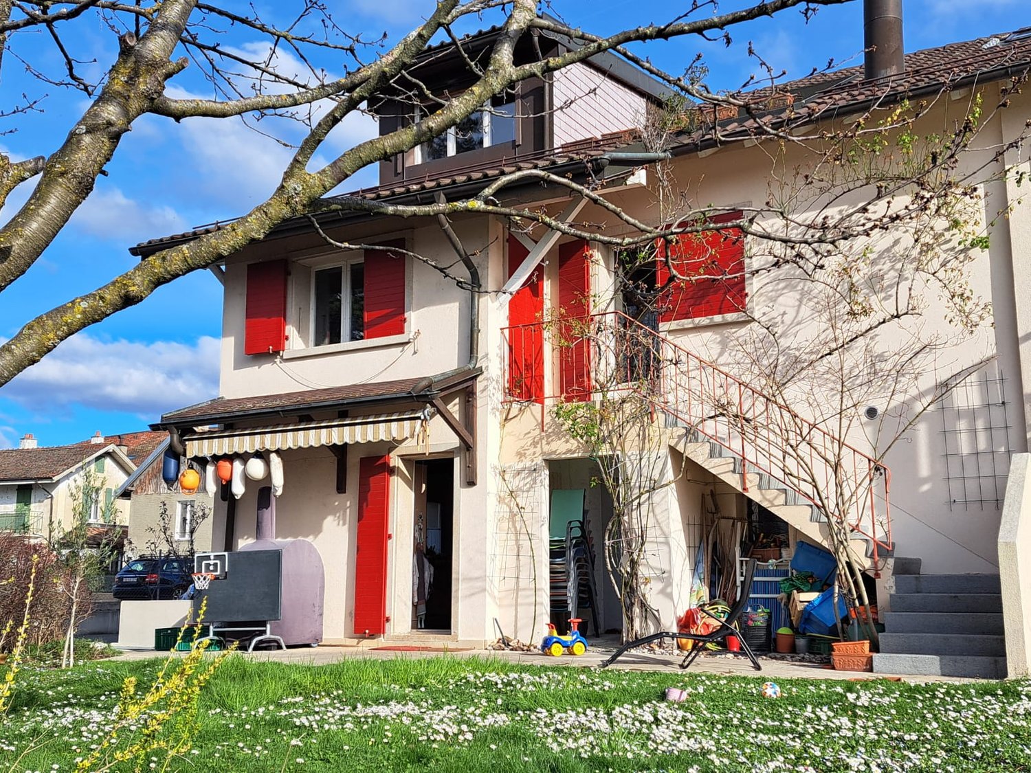 Two-story house with red and white exterior, large windows, balcony, and a garden with grass and flowers in the front yard