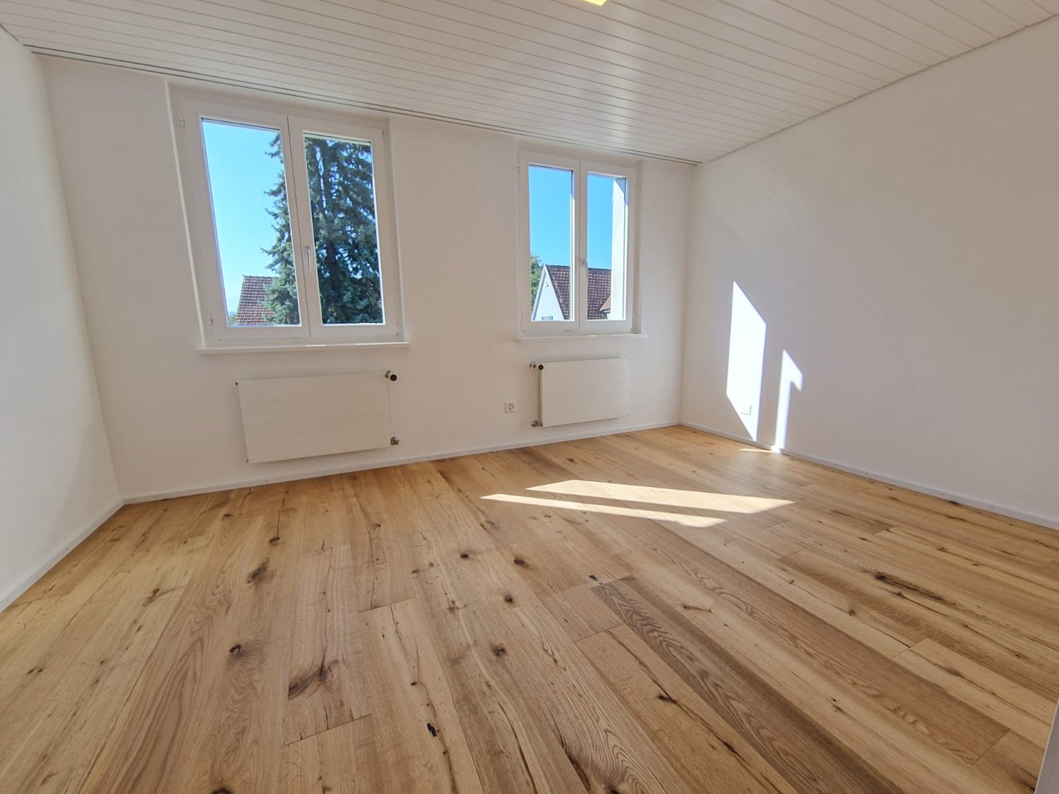 empty room with hardwood floor, large windows, white walls, radiators