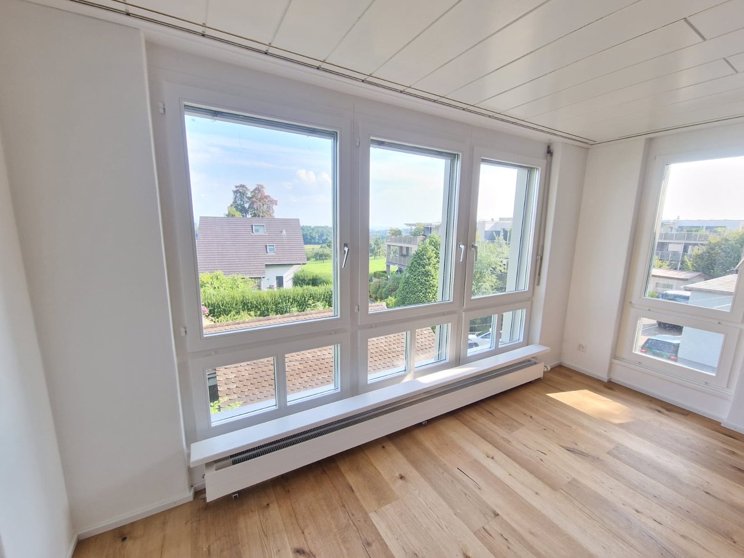room with white walls, wooden floor, large windows with a view of the outside landscape