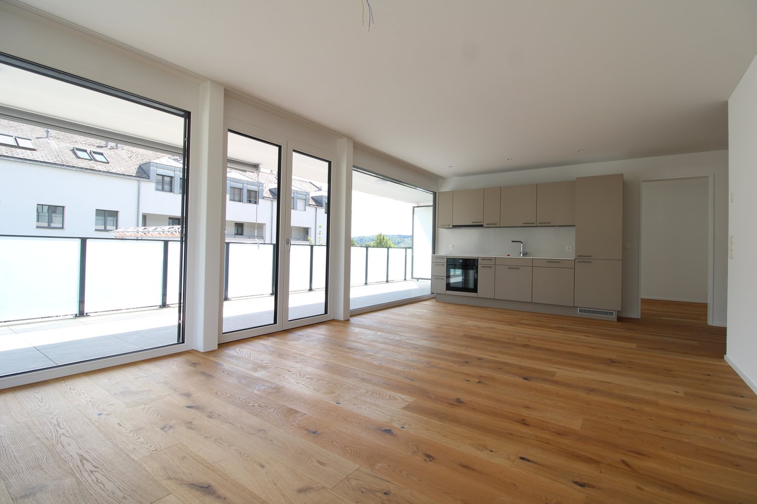 spacious interior room with large sliding glass doors leading to balcony, modern kitchen, hardwood floors