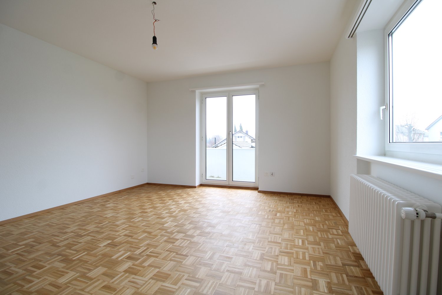 empty room with sliding glass door, wooden parquet flooring, white walls, sliding glass door, window, radiator