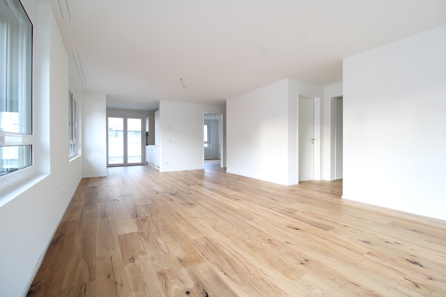 empty room with white walls, hardwood floors, large windows, and doors