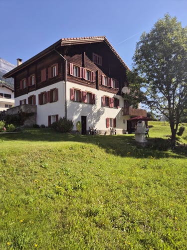 2 story house, brown and white, red shutters, large lawn, tree, mountains in the background