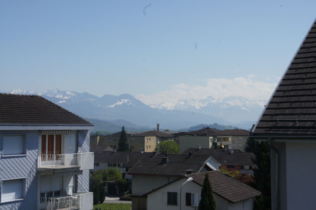 Aerial view of a residential area with snowy mountains in the distance, a blue sky, and greenery.