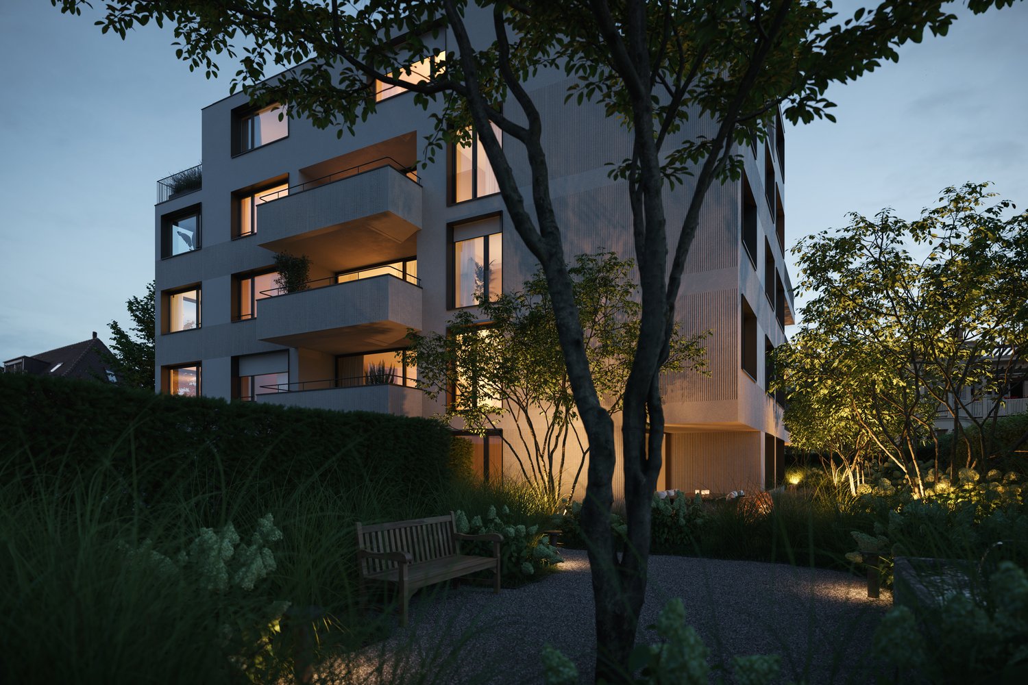 Multi-story apartment building with balconies, surrounded by trees and landscaped garden area with a bench. The building has a modern, angular design with large windows and lighting visible at night.