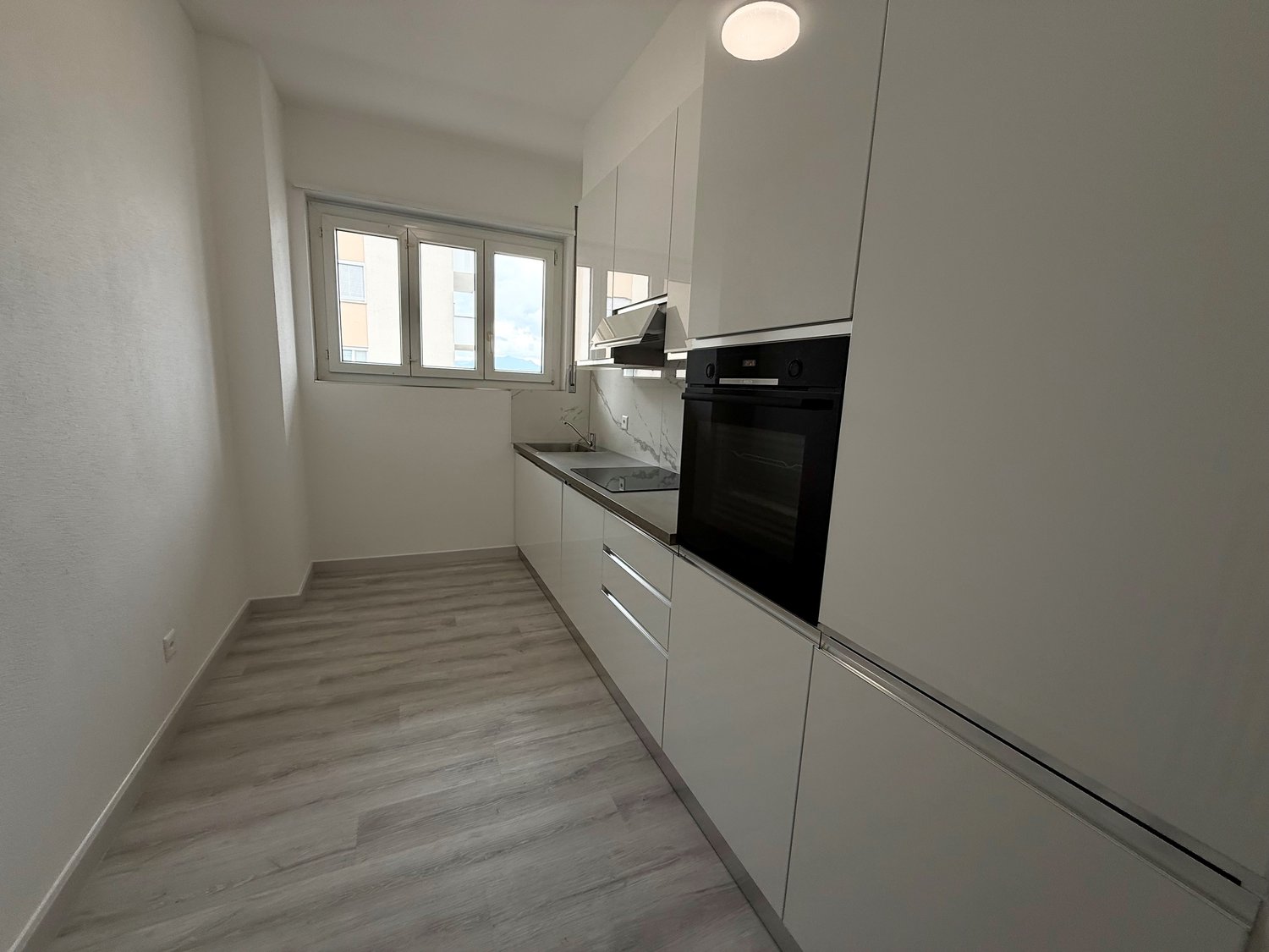 Modern kitchen with integrated appliances and white cabinets, wooden floor, and a window.