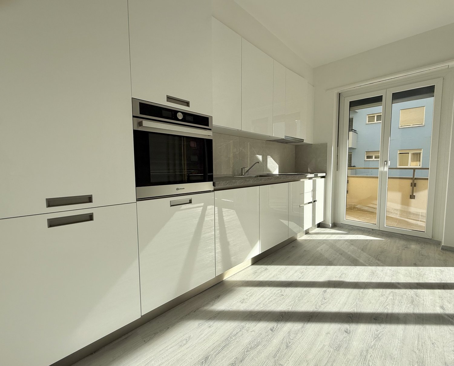 modern kitchen, white cabinets, stainless steel oven, white marble countertop, glass door leading to balcony, bright light