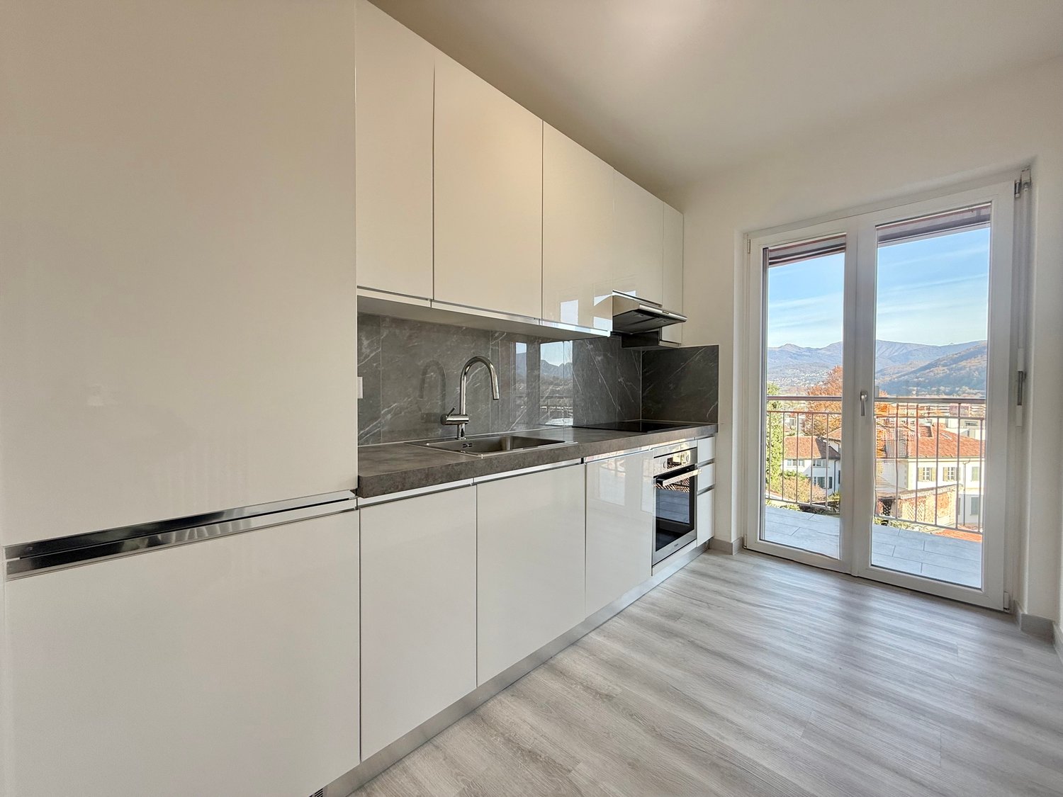 modern kitchen, white cabinetry, granite countertop, stainless steel sink, modern appliances, sliding glass doors, balcony with view