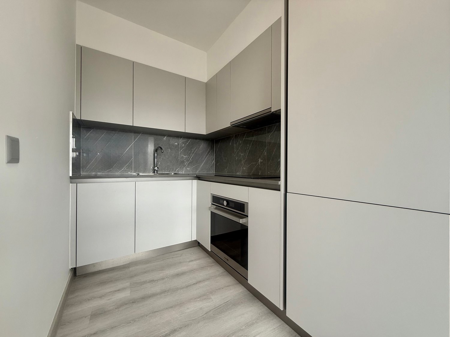 modern kitchen with white cabinets, marble countertops, built-in oven, and sleek faucet