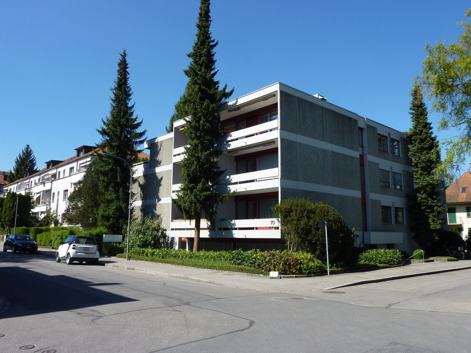 Building with three floors, multiple balconies, green spaces in front