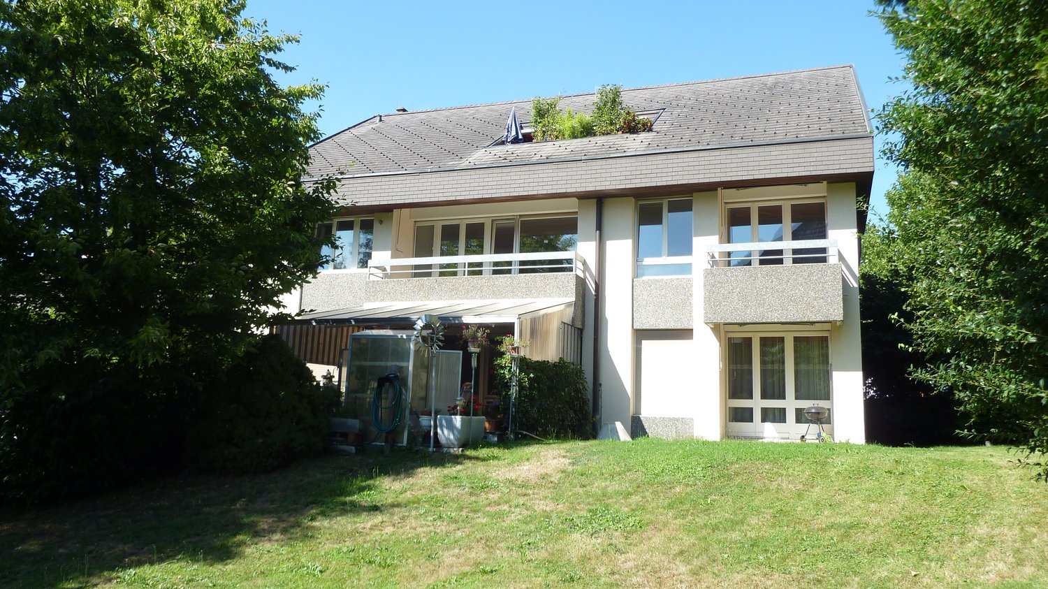 Modern house, gray roof, white walls, glass windows, balcony, plants, garden with grass