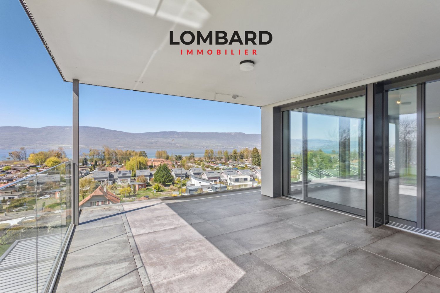 Terrace with large glass walls, tiled floor, balcony, lake view, distant houses, mountains