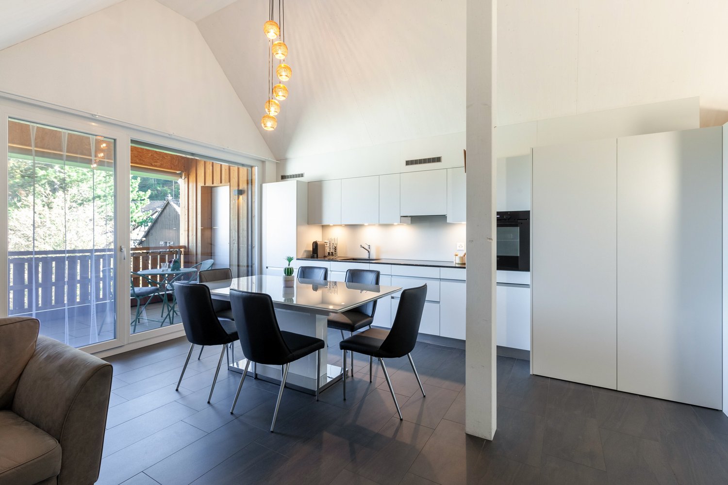 white kitchen with dining table and chairs, large glass door leading to balcony, chandelier hanging over table