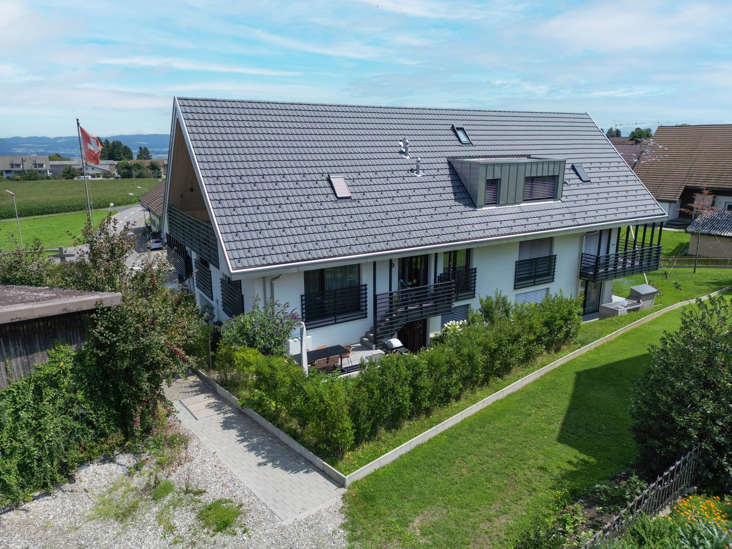 Modern house with gray roof, white walls, large windows, balconies, and a garden in a scenic area