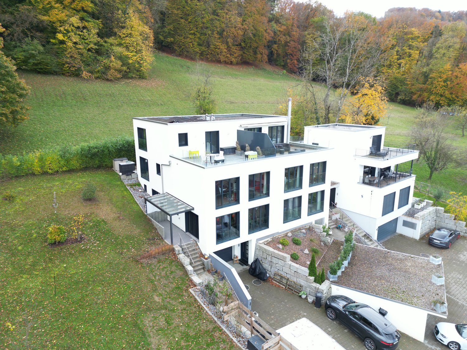 modern house with two floors, garage, 2 cars parked, landscaped garden, view of a hill