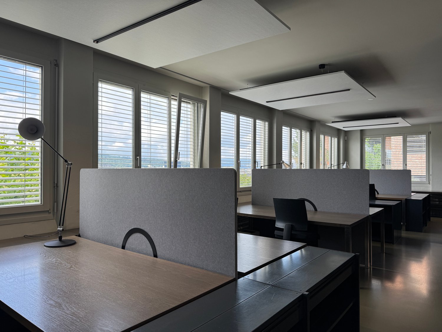 modern office with desks, chairs, lamps, large windows, gray walls, wooden floors