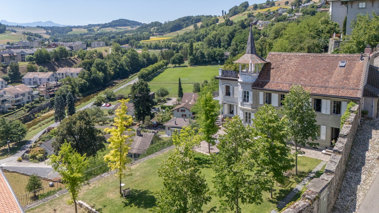 Aerial view of a large villa with red tiled roof, overlooking a beautiful landscape with houses, fields, and trees