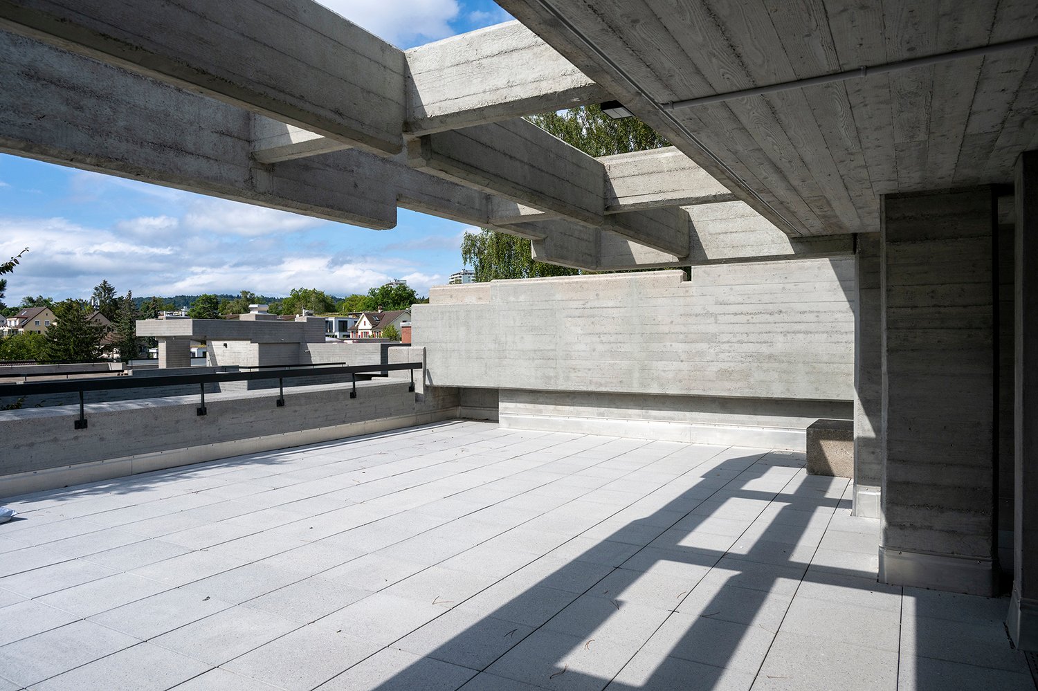 Exposed concrete beams, tiled floor, metal railings, shadows cast by beams