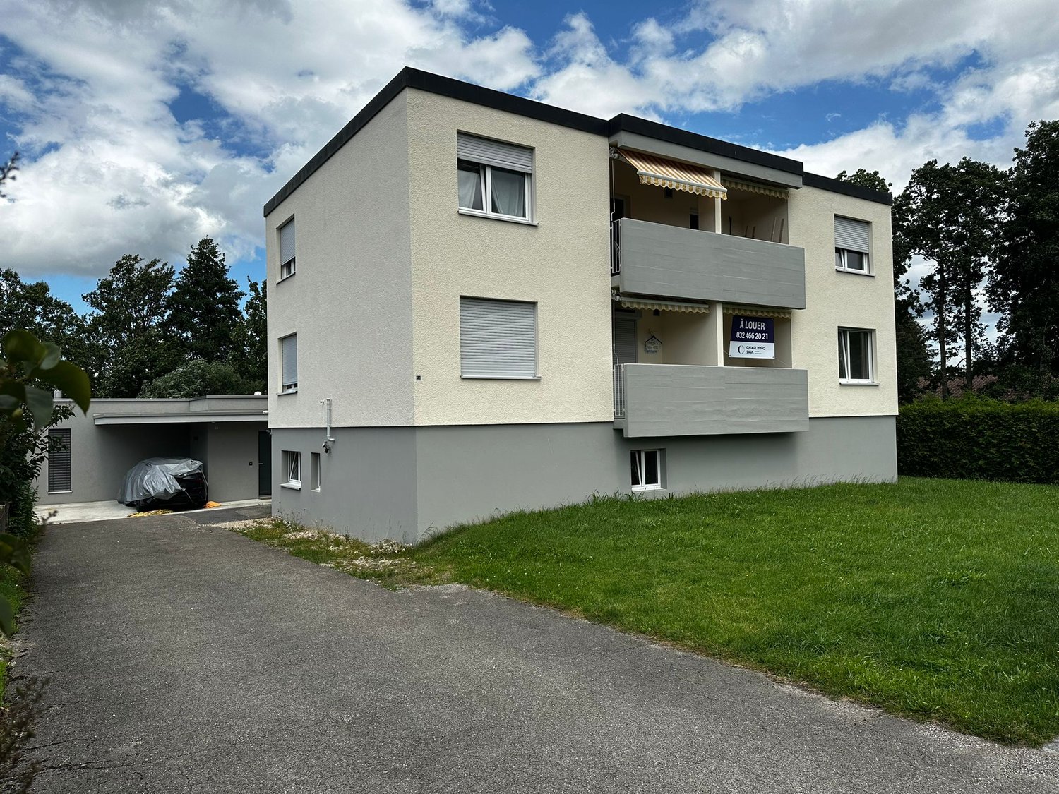 3-story apartment building with gray exterior, balconies, and a parking area in front