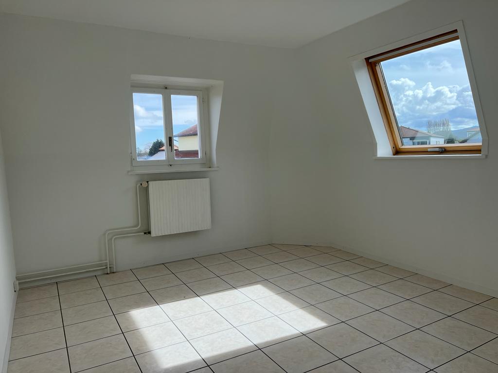 Empty room with white walls, tiled floor, and two windows providing natural light. The room appears to be a living space or bedroom.