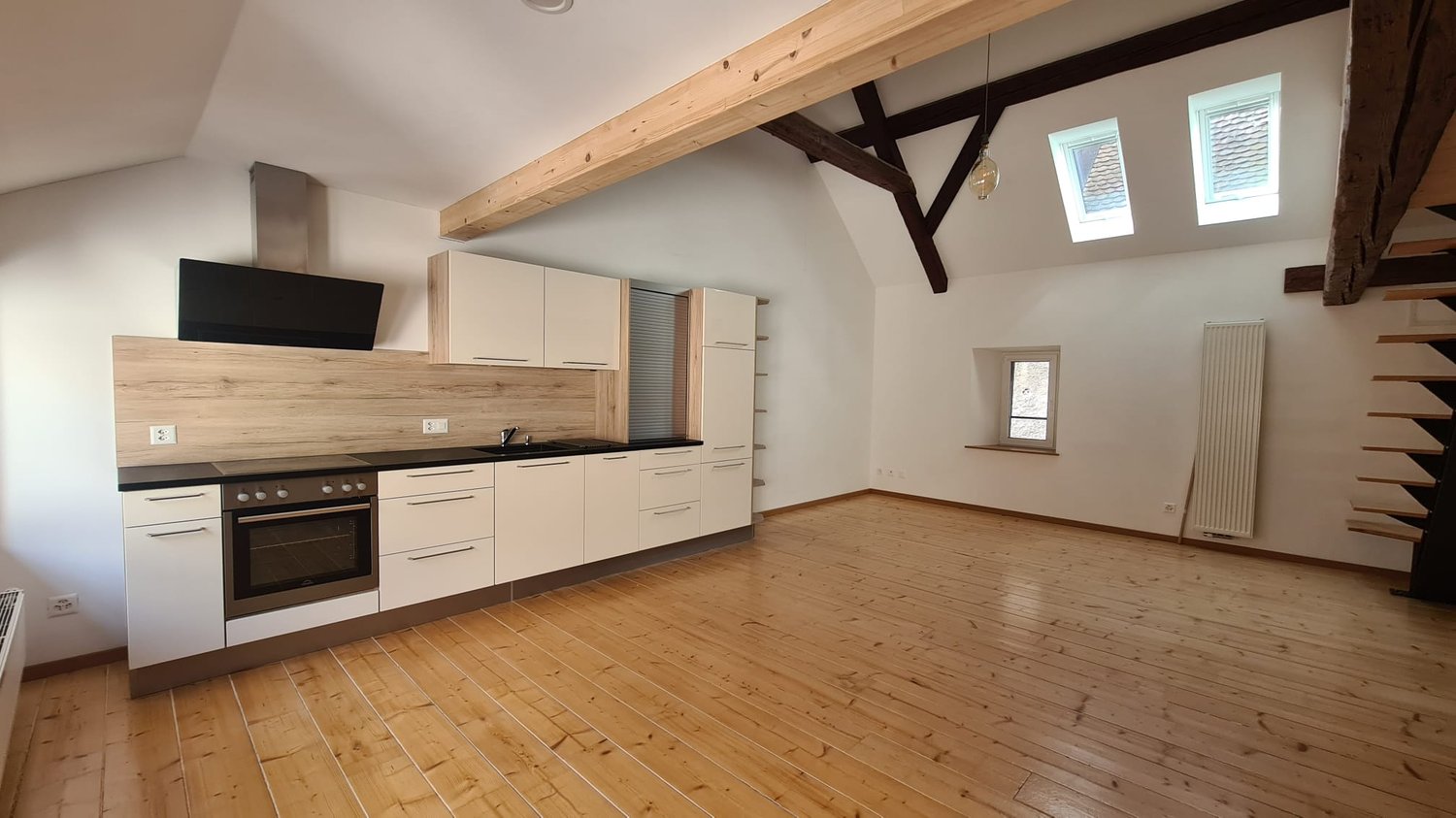 empty kitchen with wooden floor, white kitchen cabinets, gas stove, windows with wooden frames, radiator