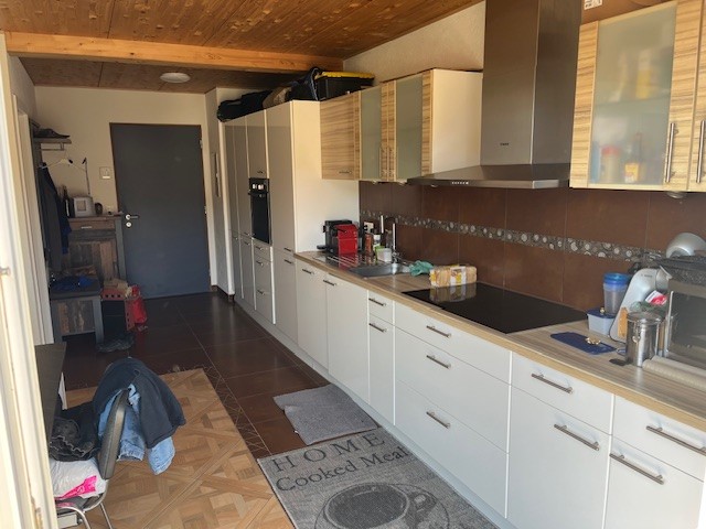 a modern kitchen with wooden ceiling, white cabinets, wooden countertop, black induction stove, brown tiled floor, and kitchen appliances