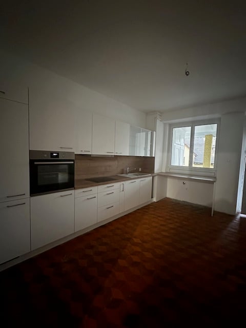 Kitchen: white cabinets, black oven, wooden floors, window with view