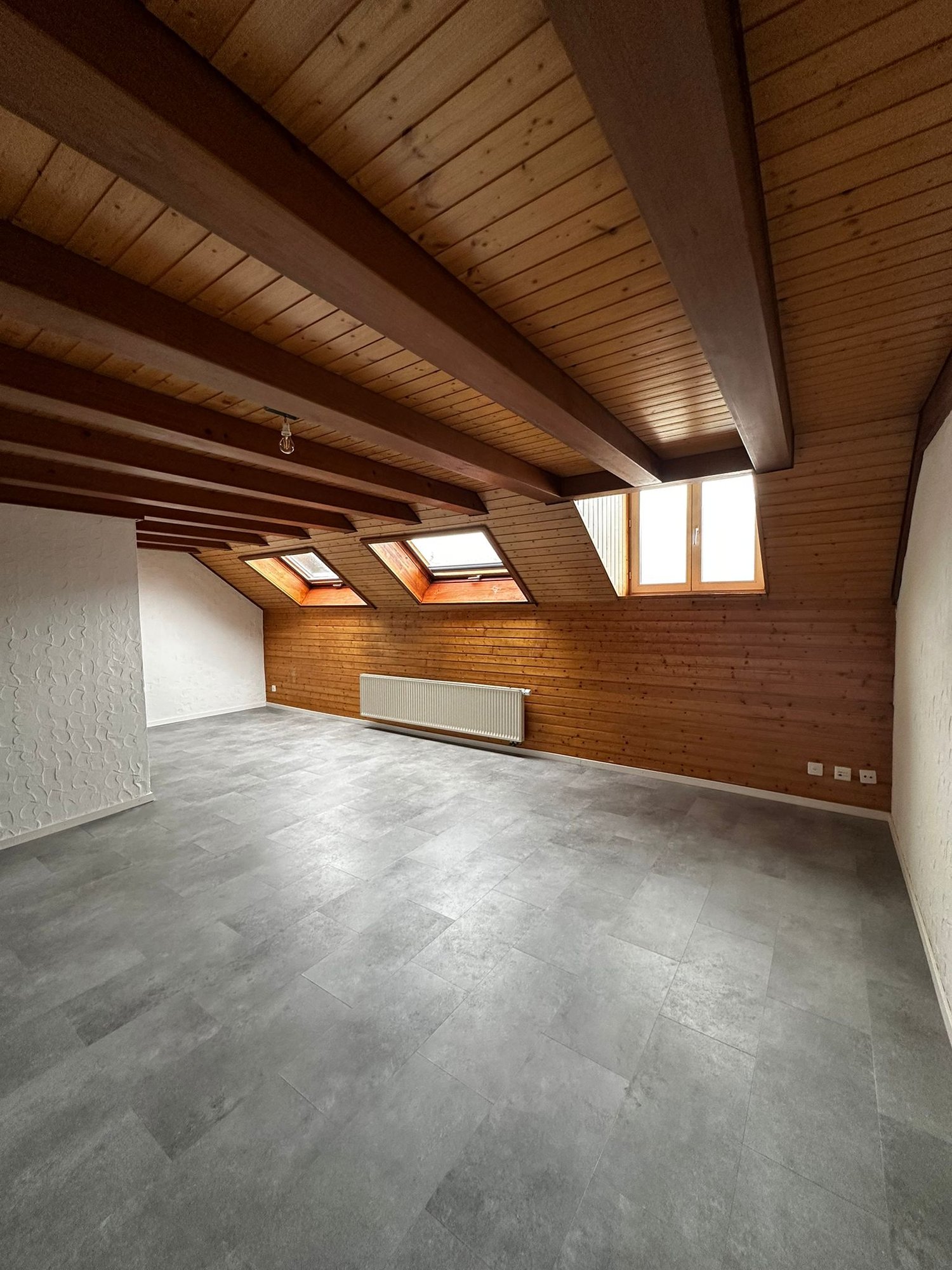 empty room, wooden ceiling, wooden walls, gray tiles, three windows, white radiator