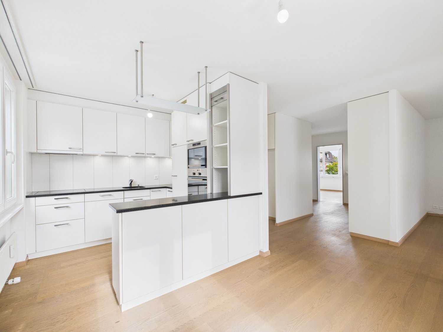 Modern kitchen with white cabinetry, black countertops, island, white walls, open concept, hardwood floors