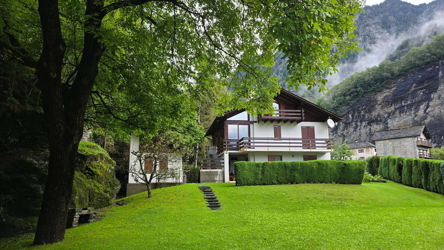 Two story house, wooden exterior, balcony, landscaped yard with shrubs and steps