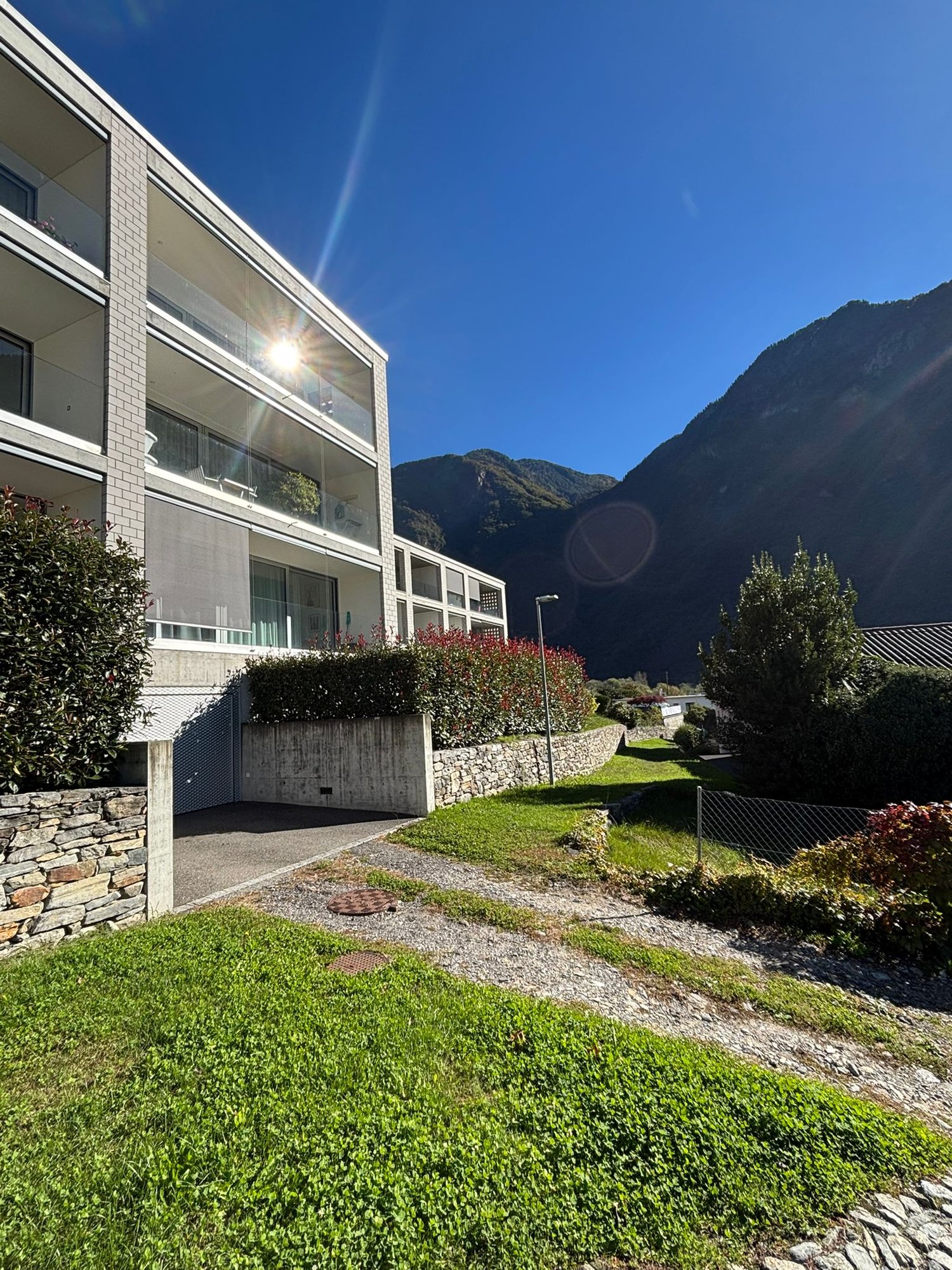 Multi-storey building, balconies, brick walls, paved entrance, well-maintained greenery