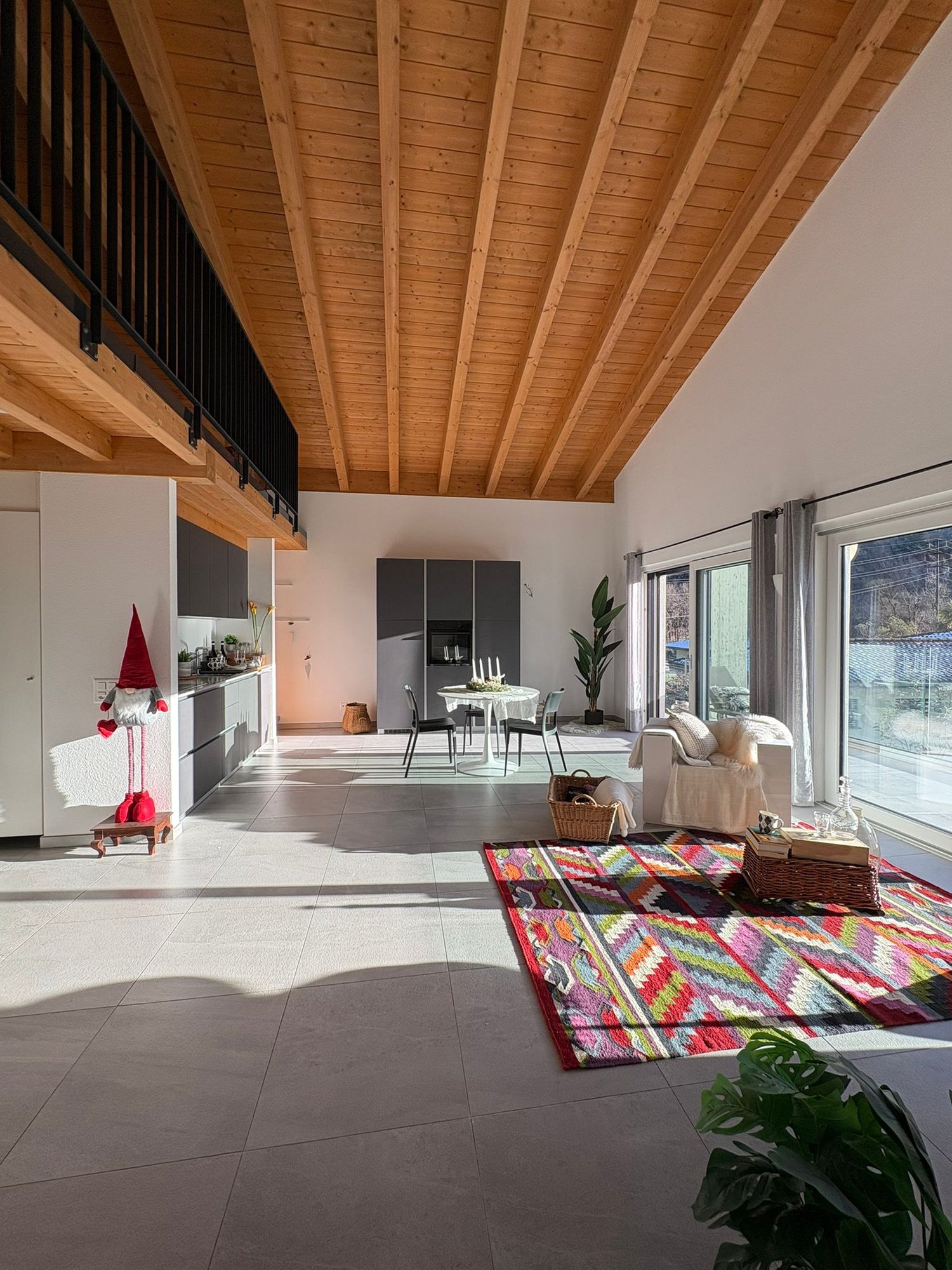 open-plan living room, large windows, balcony, wooden ceiling, dining table, kitchen, couch, rug, plants