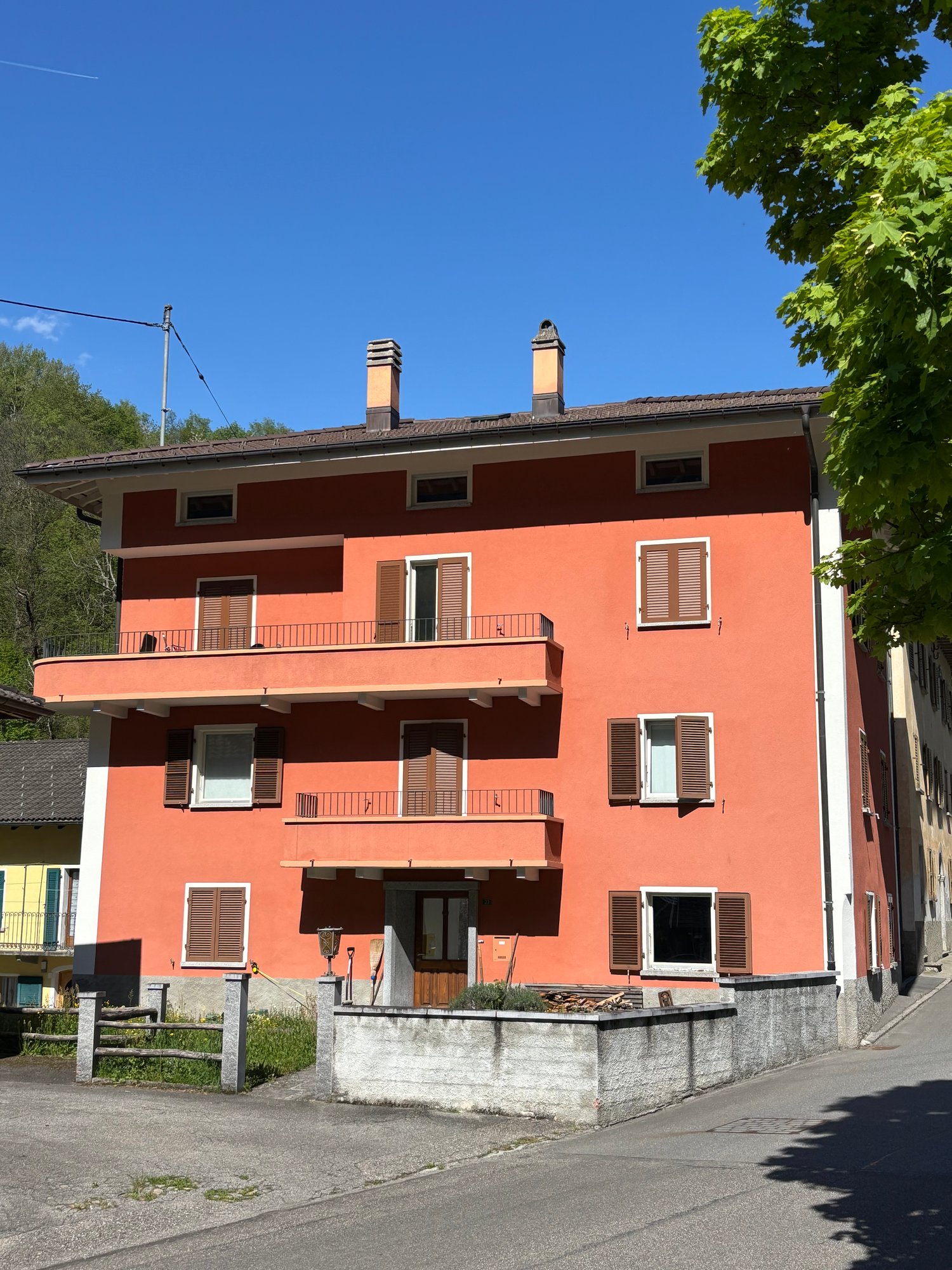 3-story apartment building with a red exterior, balconies on each floor, and chimneys on the roof.