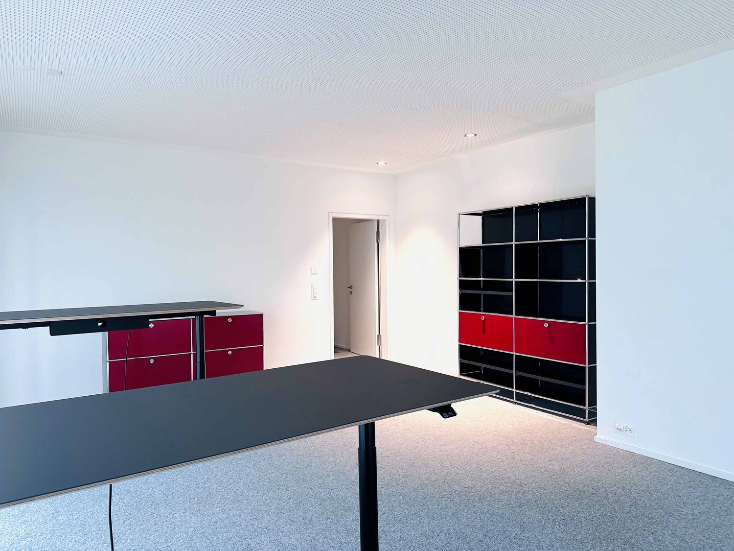 empty room, white walls, gray floor, black desk, red and black cabinets, black and red shelves
