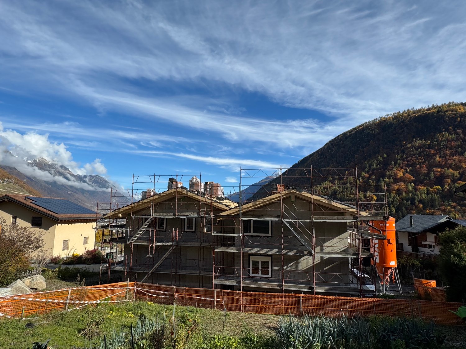 House under construction, scaffolding around, solar panels on neighboring house, mountainous background
