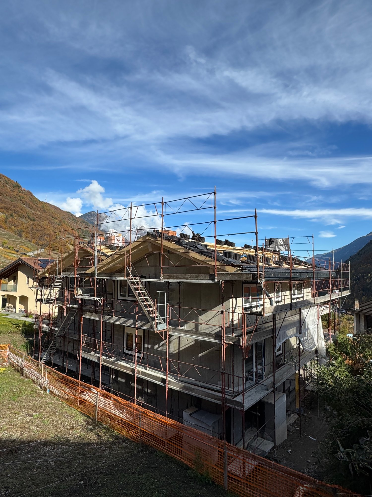 a two story house under construction, surrounded by orange fences and scaffolding